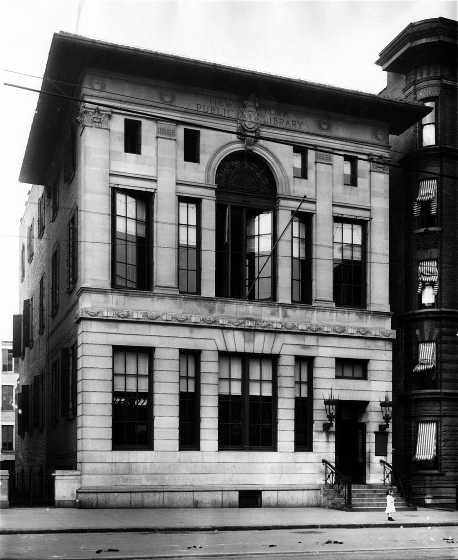 The 135th Street Branch of the New York Public Library around 1915: a three-story limestone building with tall arched windows, a child standing by the steps.