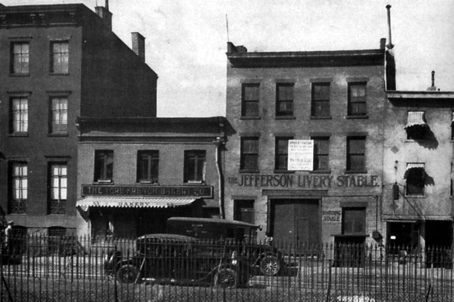 51 and 53 Christopher Street in 1928: two low brick buildings behind an iron fence, a car parked in front.