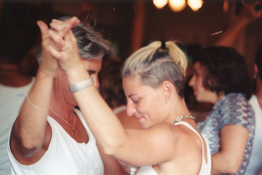 Two women hold hands and dance in a crowded room, 1997.