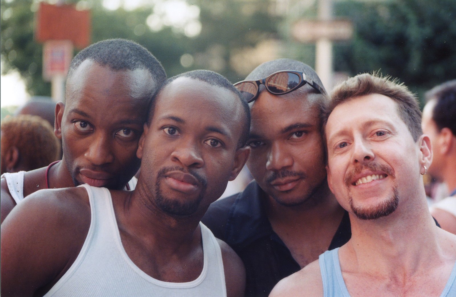 Four men crowd into the frame, grinning, their arms around each other at the Pride march.