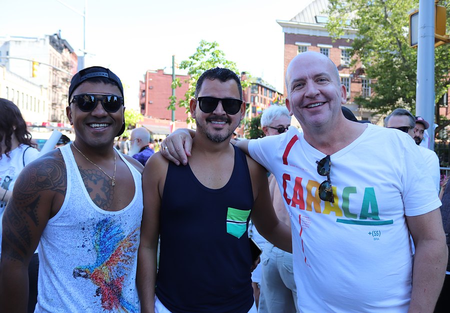 Three friends with their arms around each other, grinning, on a Greenwich Village street in June.